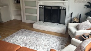 Ein Wohnzimmer mit Kamin, einem darüber montierten Fernseher und einer Couch mit gemusterten Kissen.