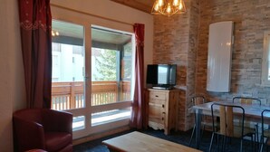 Ein Zimmer mit Holztisch, Fernseher auf einer Kommode, einer Couch und einem Essbereich mit Stühlen.