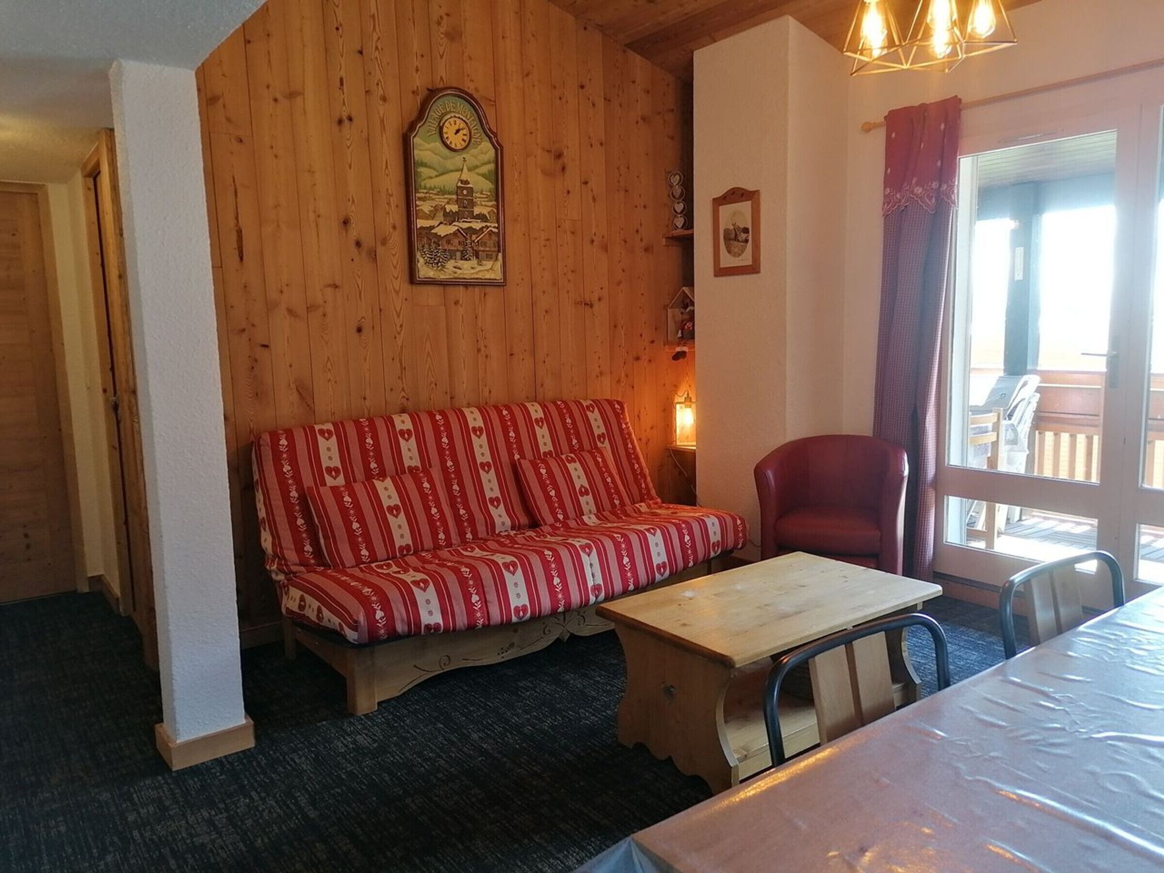 Une pièce chaleureuse avec un mur en bois, un canapé à motifs rouges et blancs, une table en bois et une chaise rouge.