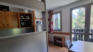 Et kompakt køkken med træskabe, en mikrobølgeovn og et lille spisebord med stole.