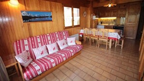 A cozy cabin interior with a wooden sofa, dining table, and kitchen area.