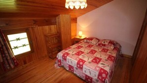 A cozy bedroom with wooden walls, a quilted bedspread, a nightstand with a lamp, and a window with star decorations.