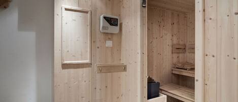 A wooden sauna room with a control panel, wooden benches, and a small shelf.