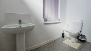 A bathroom with a white sink, a toilet, a window with blinds, and a mat on the floor.