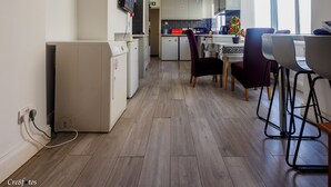 A modern kitchen with a dining area, wooden flooring, and a TV mounted on the wall.