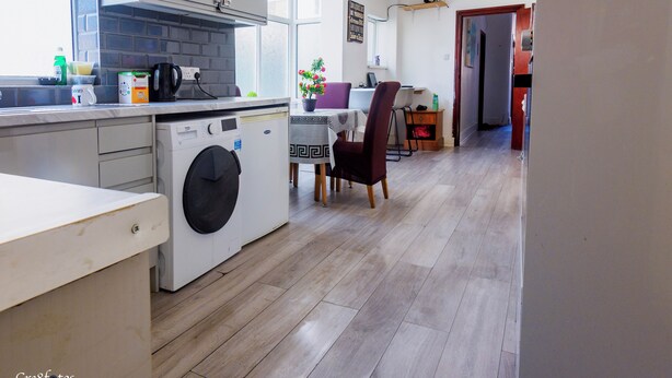 A modern kitchen with a washing machine, a dining area with a table and chairs, and a hallway leading to another room.