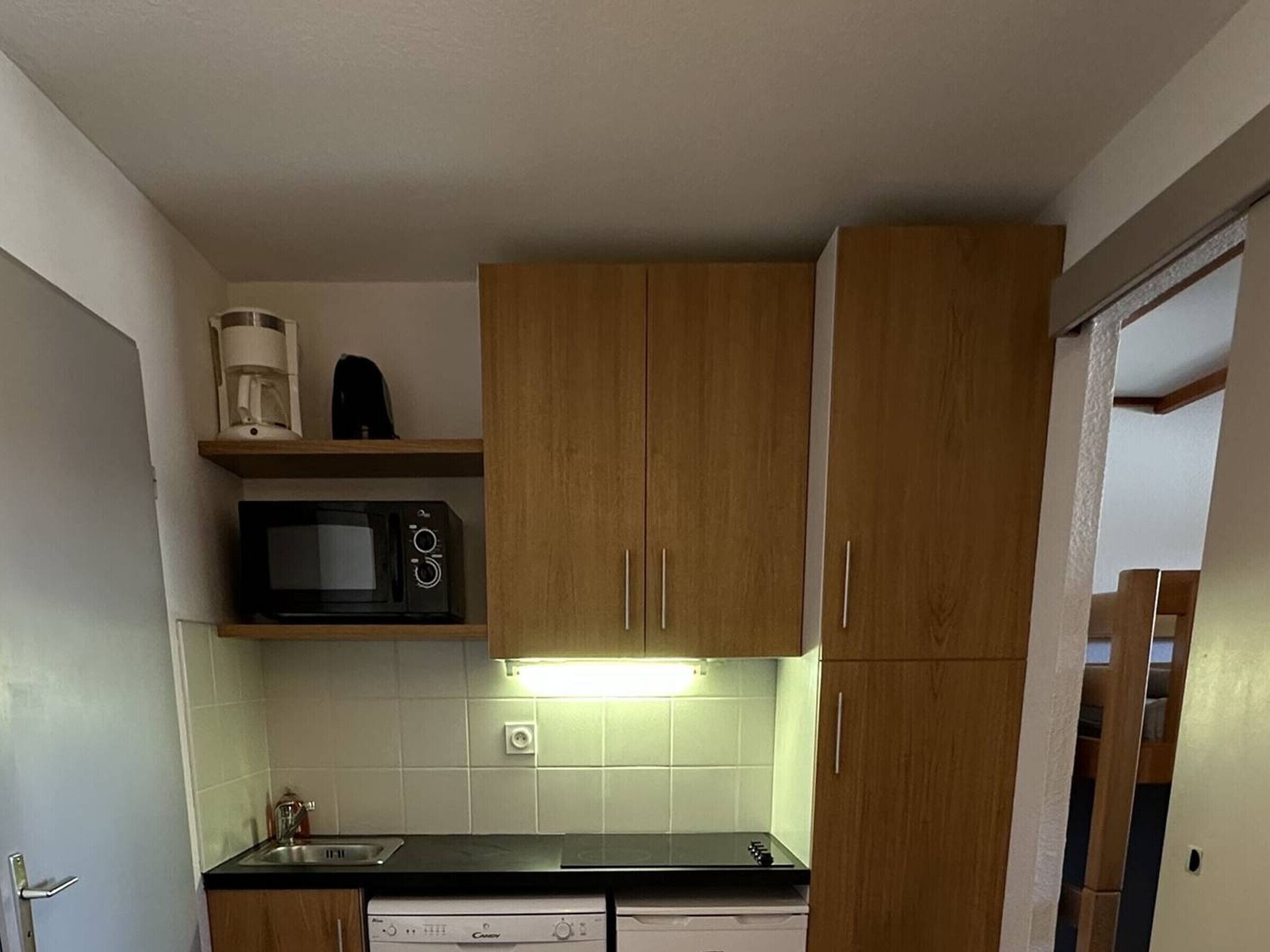 Una cocina compacta con armarios de madera, microondas, cafetera y lavavajillas.