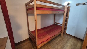 Ein Stockbett mit roter Matratze in einem Zimmer mit Holzboden und weißen Wänden.