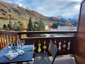 Ein Balkon mit gedecktem Tisch für zwei Personen, mit Blick auf eine Berglandschaft im Herbstlaub und einer Ansicht einer Stadt darunter.