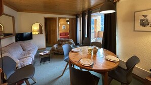 A cozy room with a wooden ceiling, a sofa, a dining table set for two, and a television on the wall. - 3-Room Alcove Apartment for 6 in Méribel, near shops (Méribel)