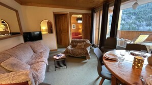 A cozy room with a sofa, a dining table set for two, and a television on the wall. - 3-Room Alcove Apartment for 6 in Méribel, near shops (Méribel)
