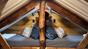 Ein Schlafzimmer im Loft-Stil mit schrägem Dach, Holzbalken und einem Bett mit gemusterten Kissen.