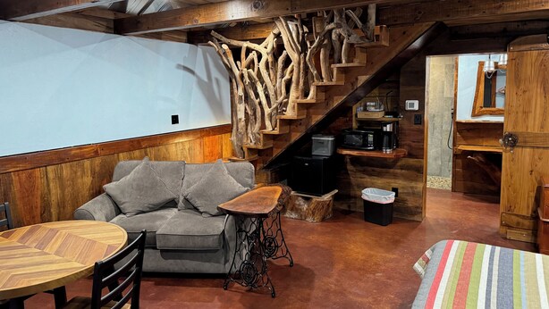 Ein gemütliches Zimmer mit einer Holztreppe, einem grauen Sofa, einem Holztisch und einer Streifen-Decke.