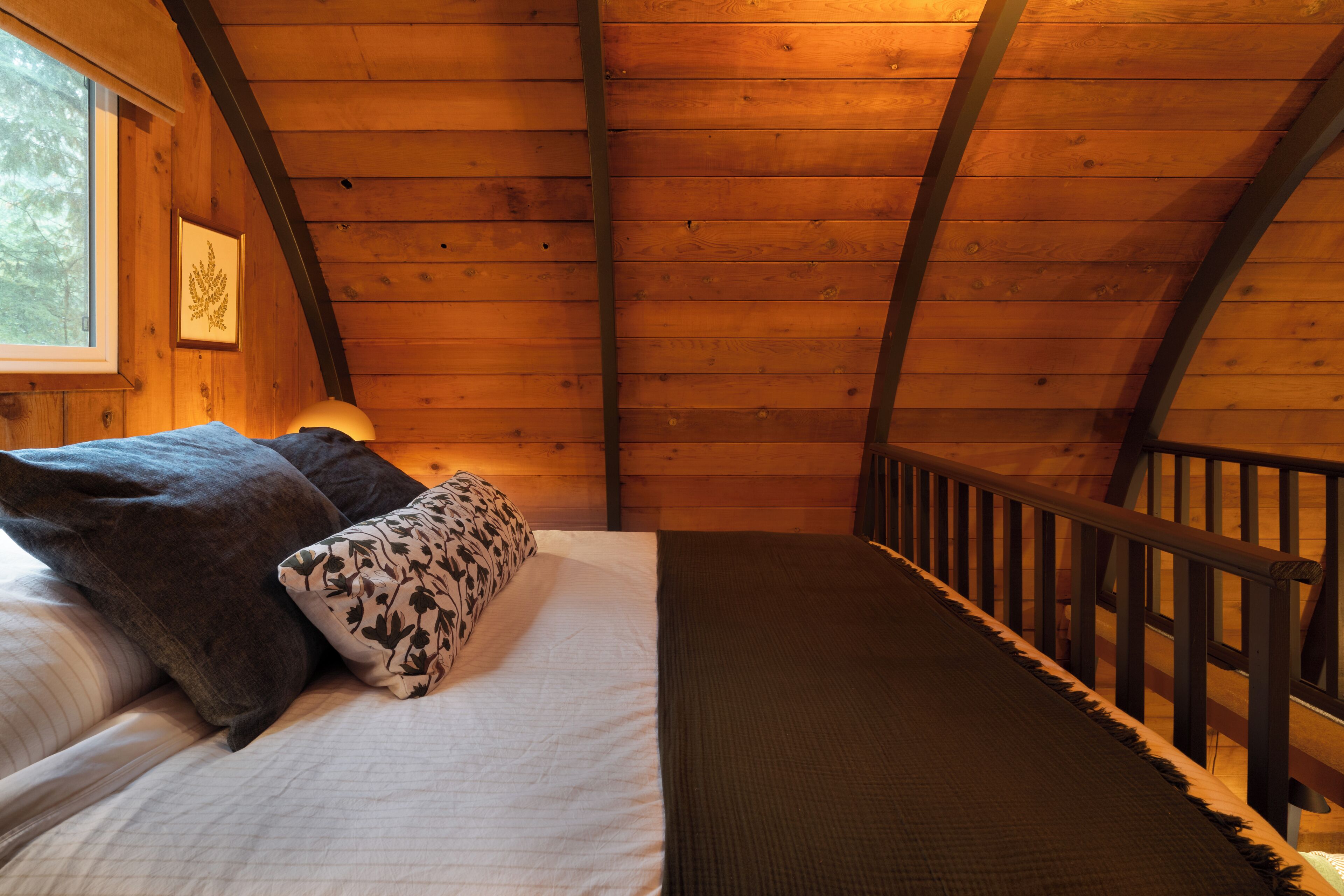 Habitación de cabaña de madera con cama, almohadas, una ventana y barandilla de madera.