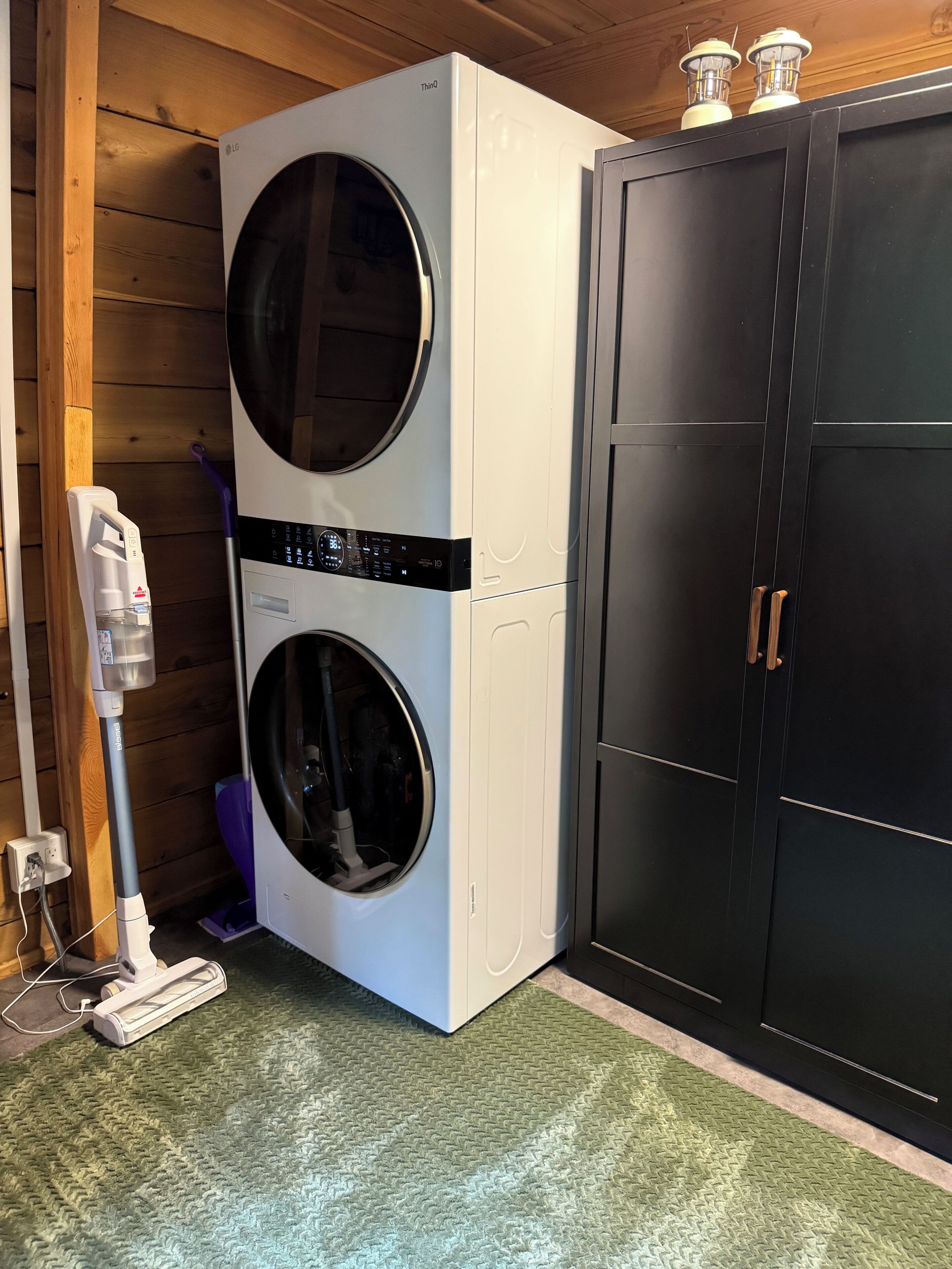 A double-door laundry room with a washing machine and dryer, a vacuum cleaner, and a cabinet.