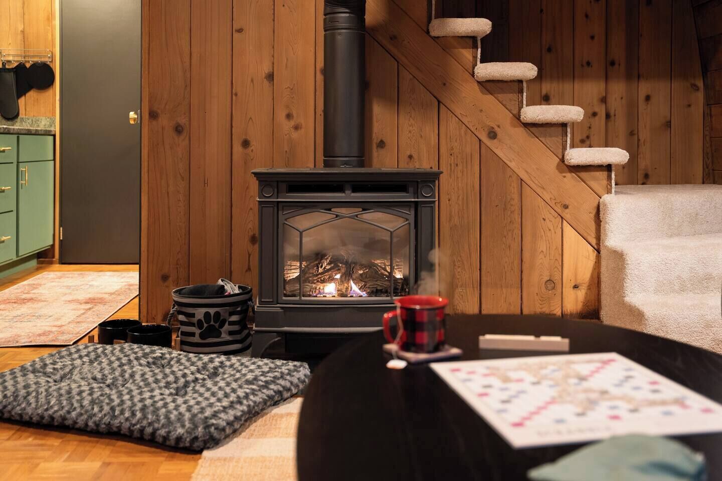 A cozy living room with a wood-burning stove, a staircase, and a dining area.