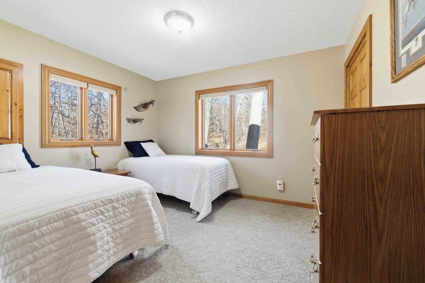 A bedroom with two beds, large windows, a wooden wardrobe, and a ceiling light.