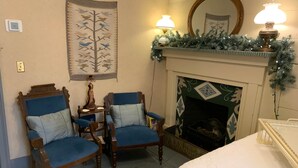 Une pièce avec une cheminée, deux fauteuils bleus, un lit et un miroir.