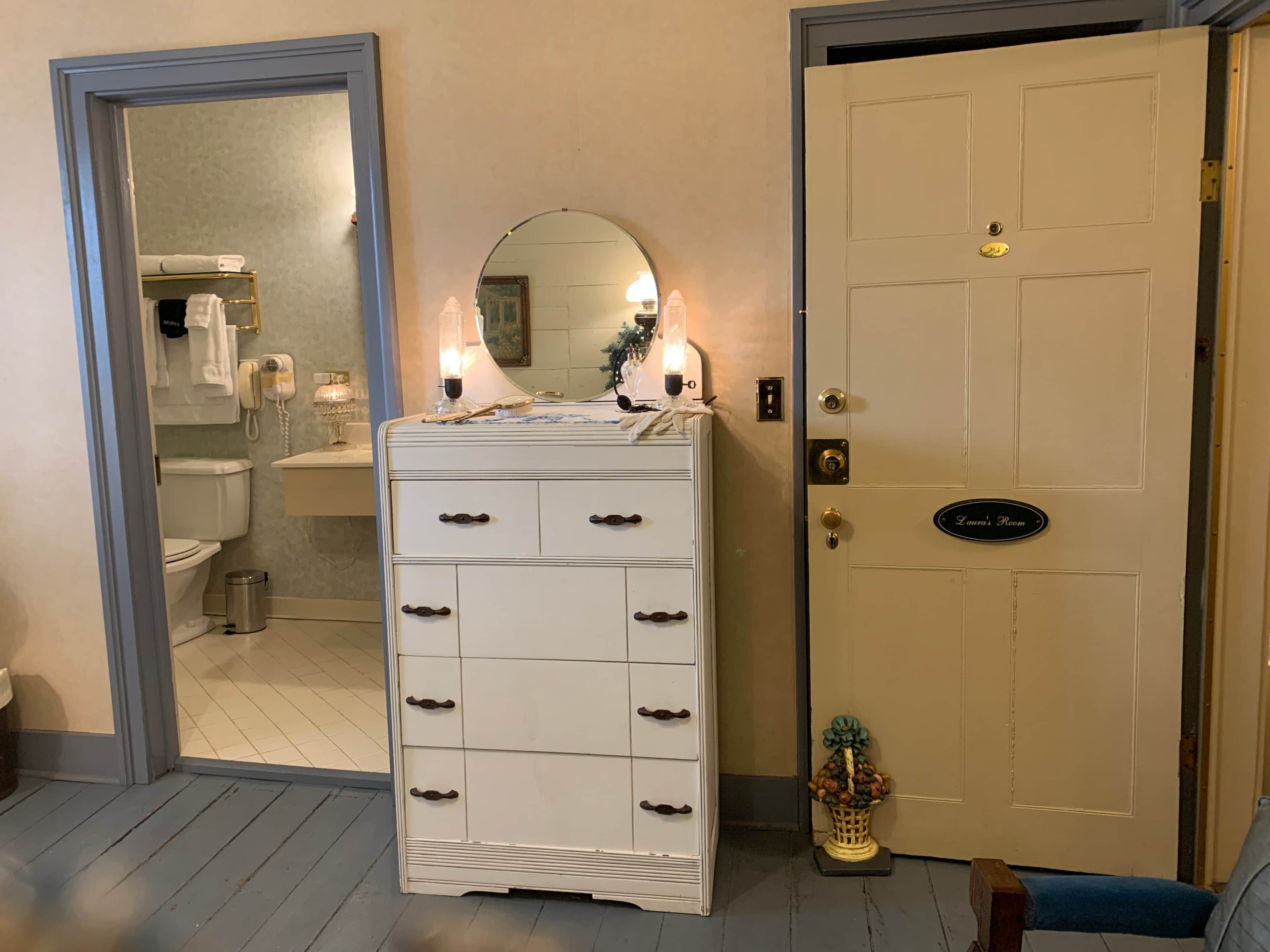 A room with a white dresser, a mirror, and a door labeled "Laura's Room".