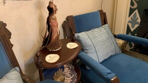 Une pièce avec un canapé bleu, une table en bois ornée d’un objet décoratif et un mur sur lequel est accrochée une tapisserie.