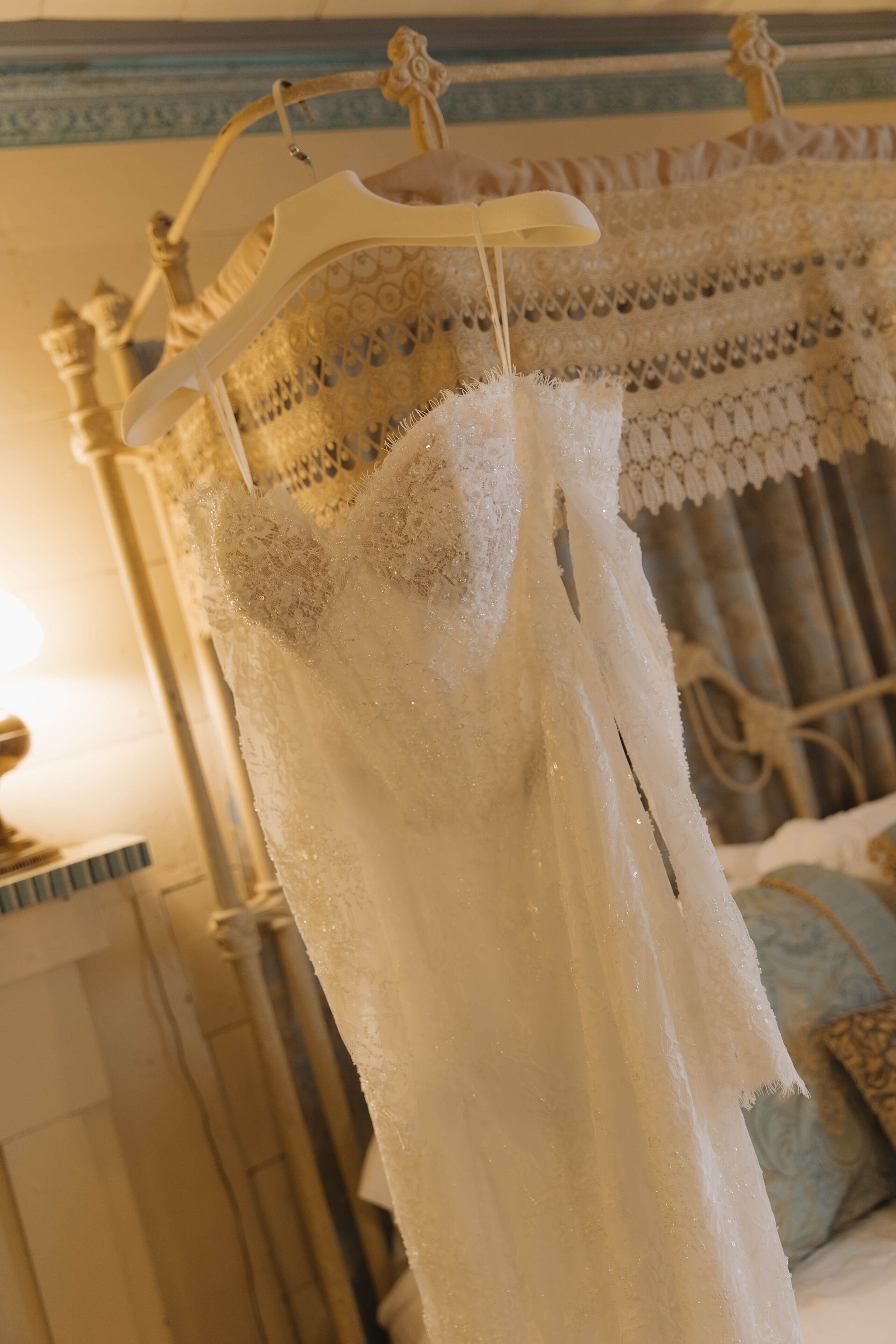A white dress hanging on a hanger in a room with a patterned bedspread and a decorative headboard.