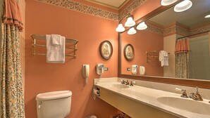 Un baño con inodoro, lavabo y espejo. Hay toallas colgadas en la pared y una cesta en el suelo.