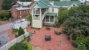 A two-story building with a green roof and a balcony. There are outdoor tables and chairs arranged on a brick patio.