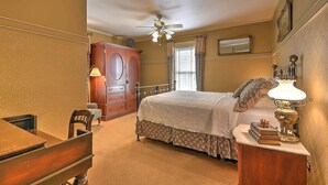 A bedroom with a bed, a wooden desk, a chair, a dresser, a ceiling fan, and a lamp. - The Russell Room at The Historic Eureka Inn and Event Center (Jonesborough)