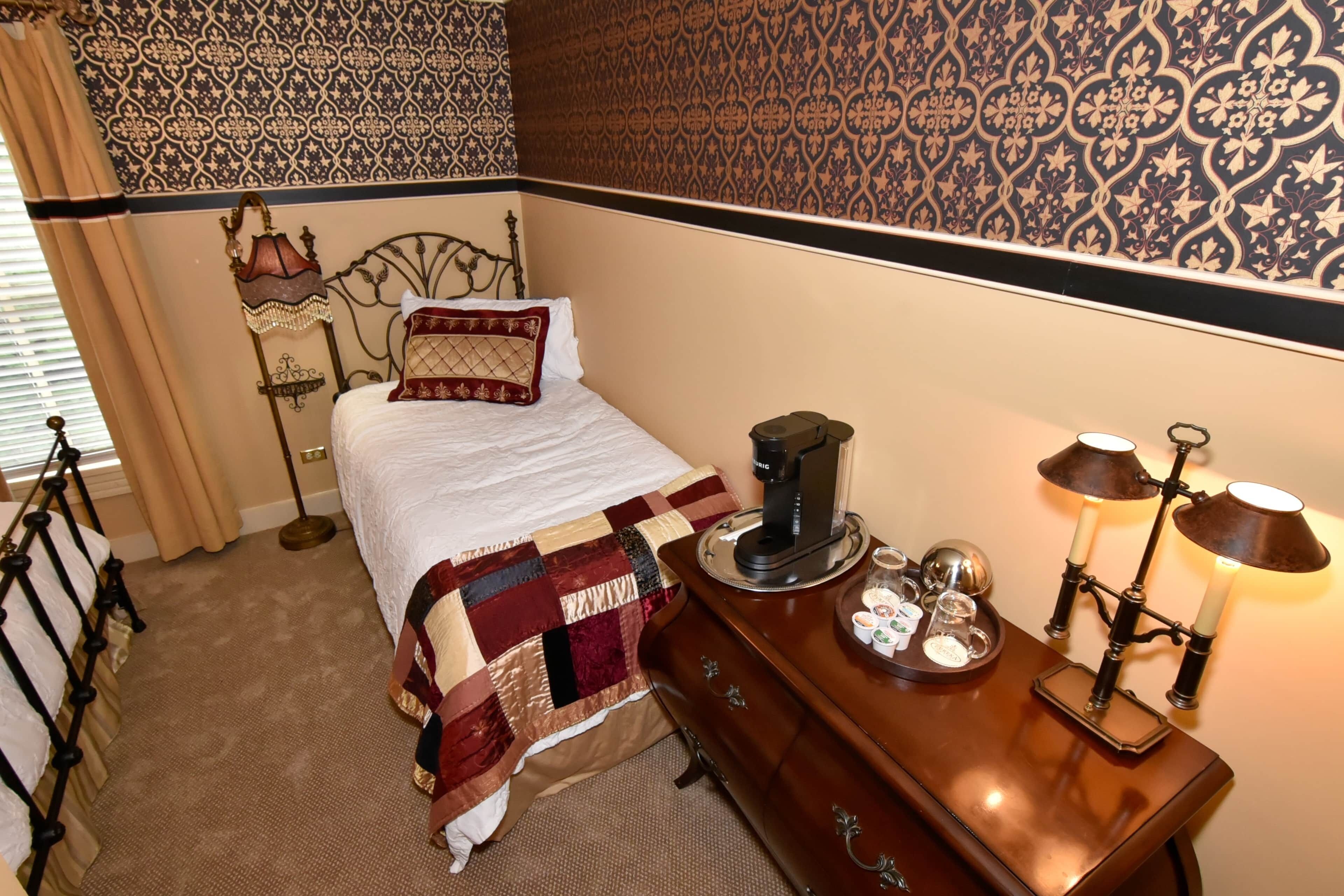 A neatly made bed with a patterned quilt, a bedside table with a lamp, and a decorative wall.