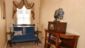 A room with a blue sofa, two lamps, a wooden side table with books, a decorative item on the table, and a window with curtains. - The Tub Room at The Historic Eureka Inn and Event Center (Jonesborough)