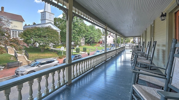 A covered porch with a railing, wooden benches, and a view of a street with parked cars and houses. - The Tub Room at The Historic Eureka Inn and Event Center (Jonesborough)