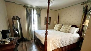Un lit à baldaquin avec un cadre en bois, une table de chevet avec une lampe et un miroir au mur.