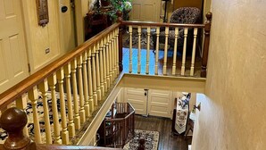 Un intérieur à plusieurs niveaux avec un escalier en bois, un coin repas avec une table et des chaises, et un salon agrémenté d’un tapis à motifs et d’un canapé.