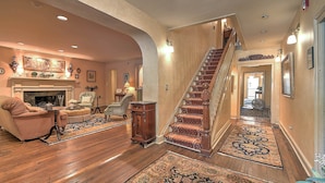 A spacious living room with a fireplace, a staircase, and a hallway leading to another room. - Angeline's Room at The Historic Eureka Inn and Event Center (Jonesborough)