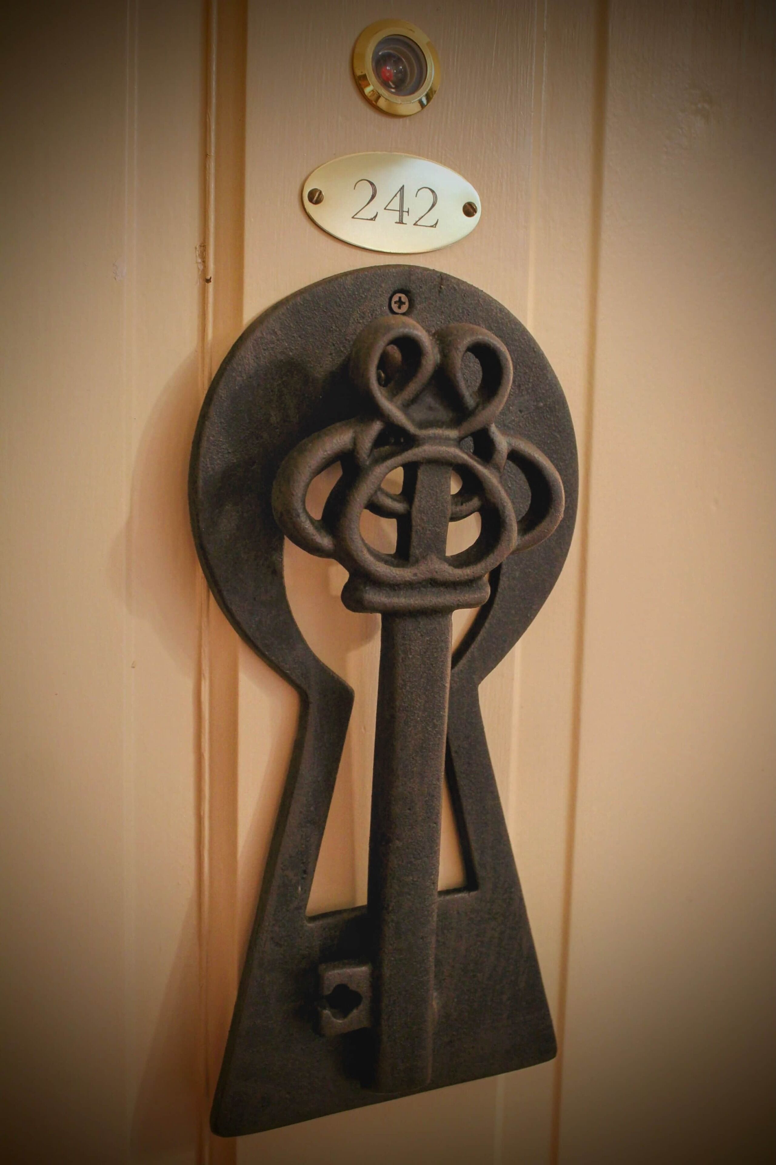 Une porte dotée d’une grande serrure décorative en forme de clé et d’une plaque avec le numéro 242.