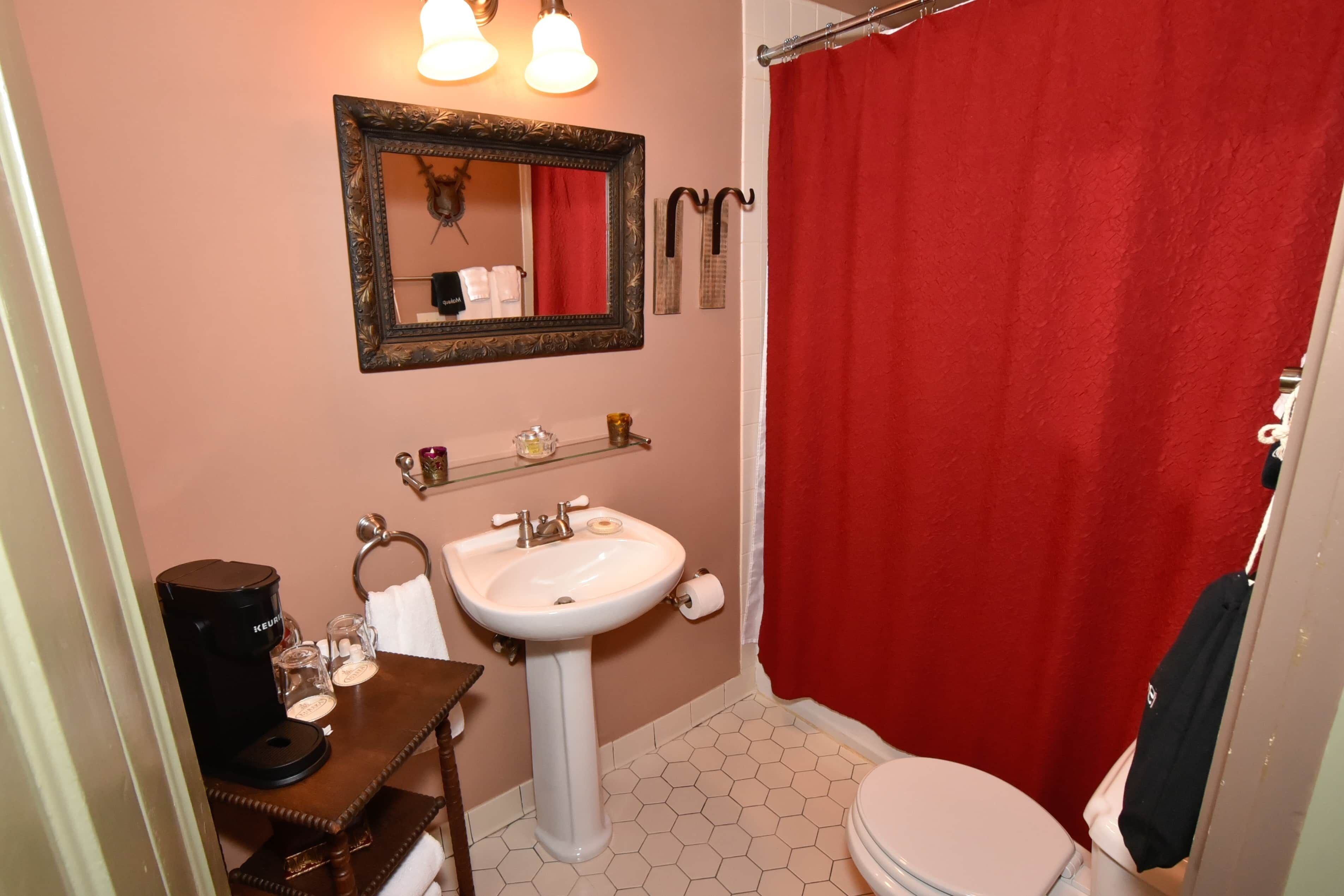 Un baño con lavamanos blanco, espejo, cortina de ducha roja y retrete.