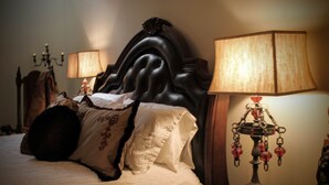 A bed with a dark headboard, multiple pillows, and a bedside table with a lamp and decorative items. - Angeline's Room at The Historic Eureka Inn and Event Center (Jonesborough)