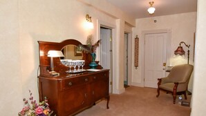 A hallway with a wooden dresser, a mirror, and a vase of flowers. There is a chair and a door in the background. - The Sample Room  at The Historic Eureka Inn and Event Center (Jonesborough)