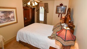 A bedroom with a large bed, a ceiling fan, a nightstand with a lamp, a wooden dresser, and a framed picture on the wall. - The Sample Room  at The Historic Eureka Inn and Event Center (Jonesborough)