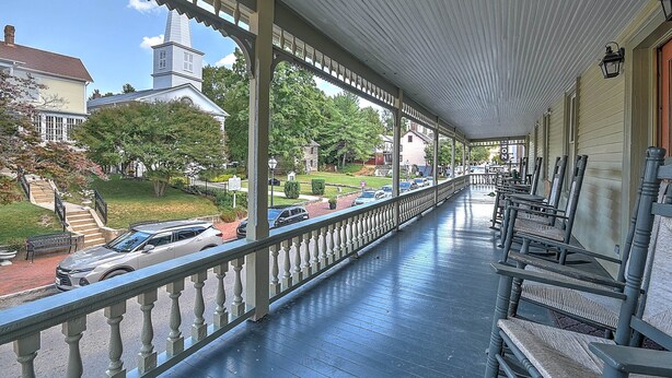 A covered porch with a railing, wooden benches, and a view of a street with parked cars and houses. - The Sample Room  at The Historic Eureka Inn and Event Center (Jonesborough)