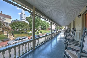 A covered porch with a railing, wooden benches, and a view of a street with parked cars and houses. - The Maxwell Room at The Historic Eureka Inn (Jonesborough)