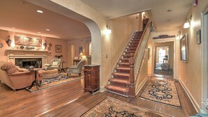 A spacious living room with a fireplace, a staircase, and a hallway leading to another room. - The Maxwell Room at The Historic Eureka Inn (Jonesborough)