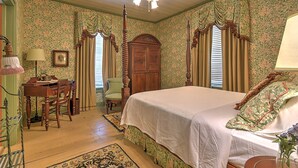 A bedroom with floral wallpaper, a four-poster bed, a desk with a lamp, and a chair. - The Maxwell Room at The Historic Eureka Inn (Jonesborough)