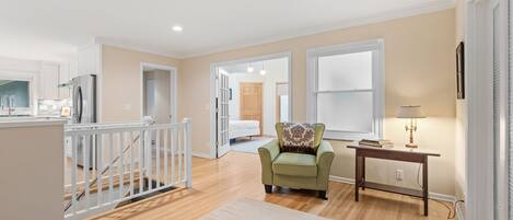 A spacious living area with a staircase, a green armchair, a wooden console table, and a lamp.