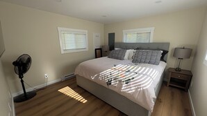 A bedroom with a bed, two bedside tables, a floor lamp, and a standing fan.