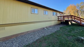 A building with a yellow exterior, a wooden staircase leading to a deck, and a gravel pathway.
