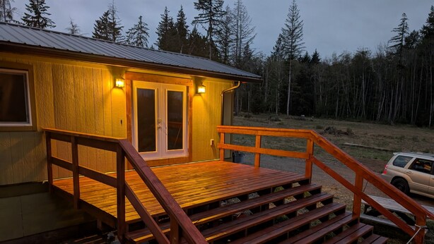 A wooden deck with a metal railing leading to a cabin with two doors and windows, surrounded by a forest.