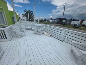 Une terrasse en bois blanc, dotée de bancs et d’une rambarde, qui offre une vue sur une zone verdoyante parsemée de palmiers et sous un ciel dégagé.