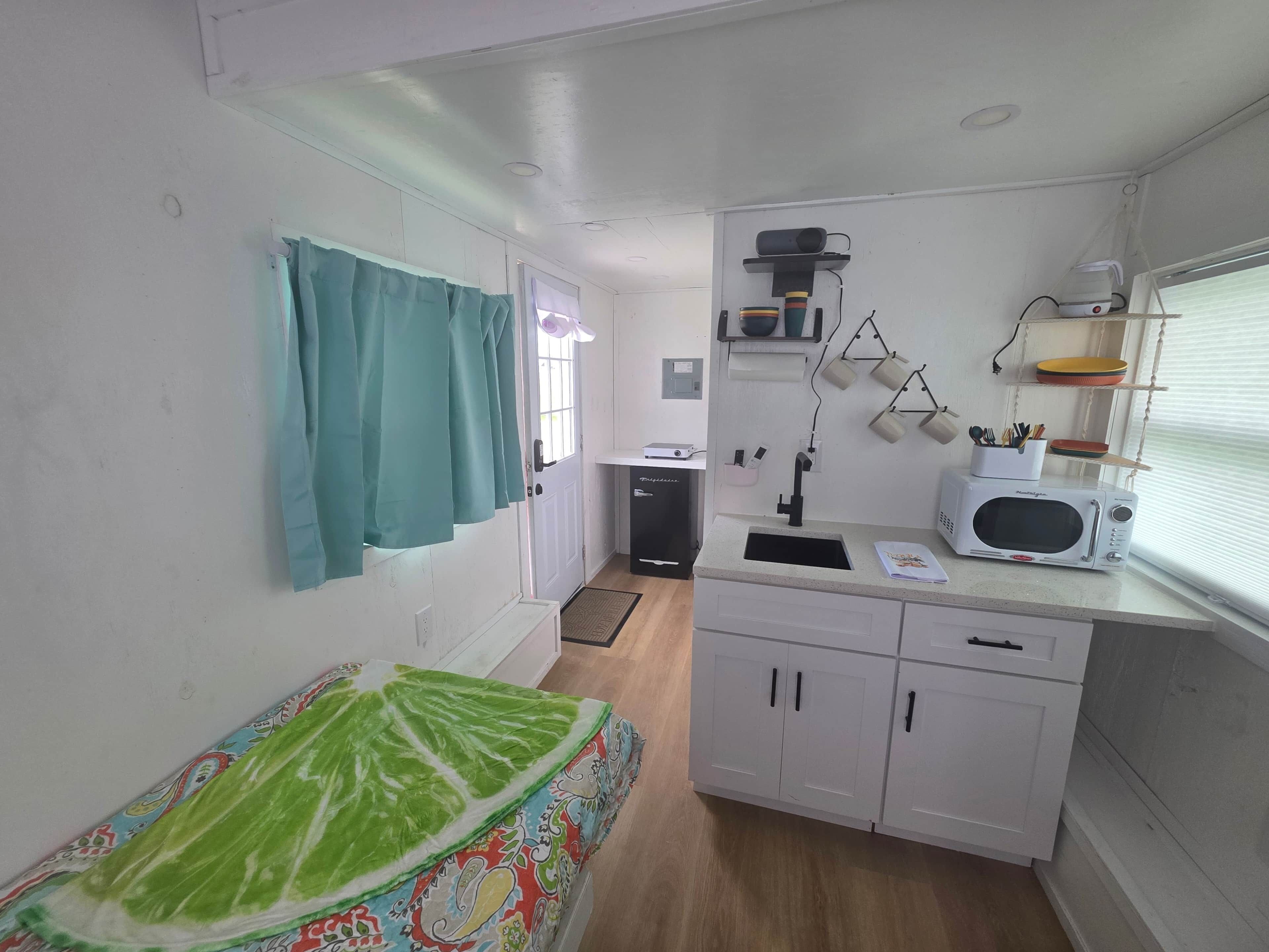 Een kleine keuken met een magnetron, spoelbak en opbergkasten.