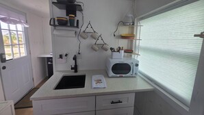 Cocina compacta con microondas, pileta y ventana con persianas.